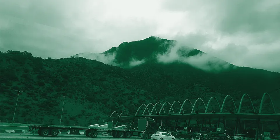 Camiones en la plaza de peaje Angostura, bajo un cerro con nubes